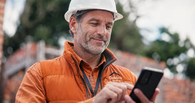 Oakline Roofing professional in an orange uniform and white hard hat using a smartphone